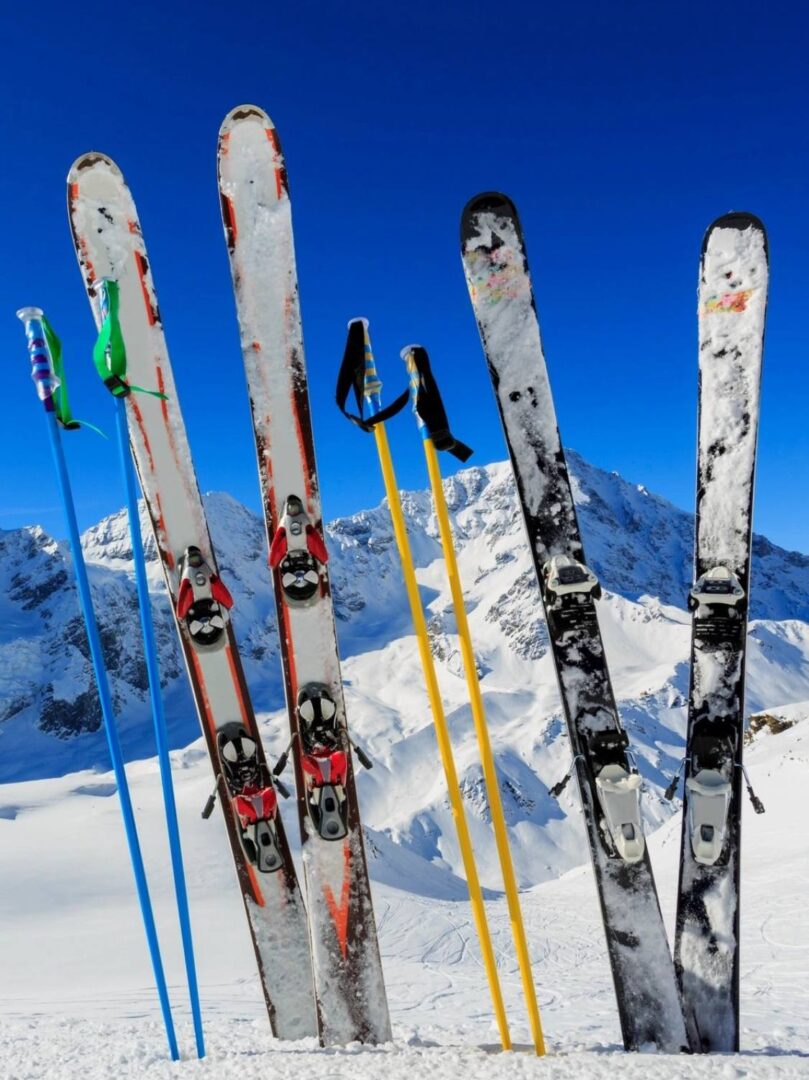 A group of skis in the snow with mountains behind them.